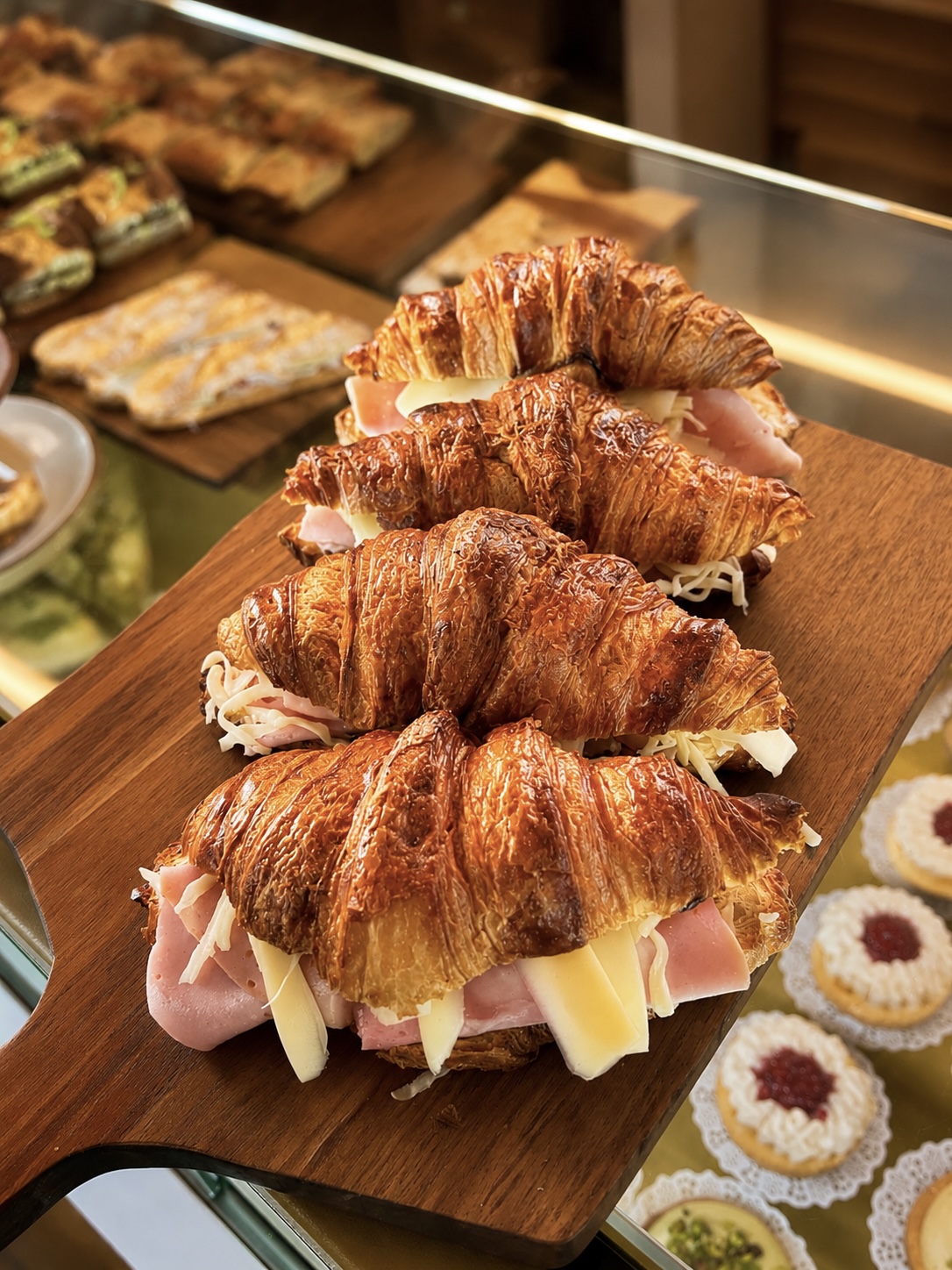 A row of ham and cheese croissants on a wooden board in the display cabinet